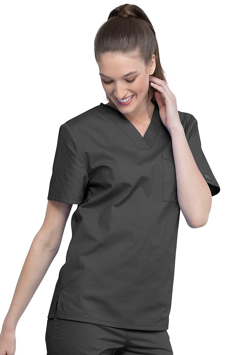 A young female Nurse Practitioner wearing a Cherokee Unisex Tuck-in V-neck Scrub Top in Pewter size Large featuring short sleeves & a V-neckline.