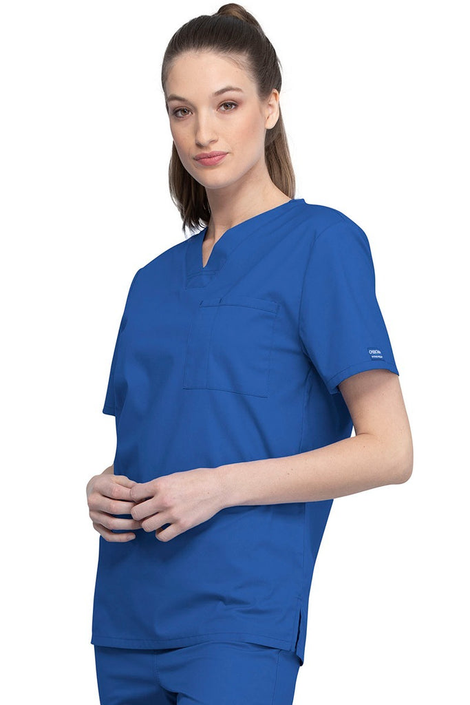 A picture of a young female Helathcare Professional wearing a Cherokee Unisex Tuckable V-neck Scrub Top in Royal  size Small featuring side slits for additional range of motion