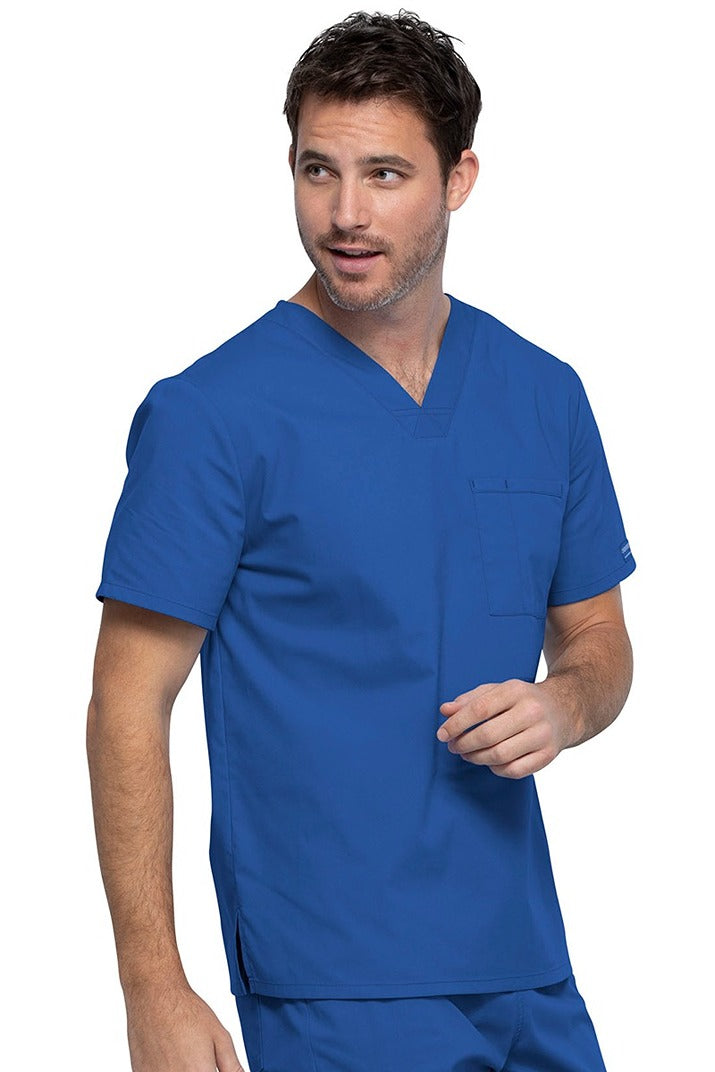 A young male Psychiatric Aide wearing a Cherokee Unisex Tuckable V-neck Scrub Top in Royal size Medium featuring one front chest pocket with a pen stitch on the wearer's left side.