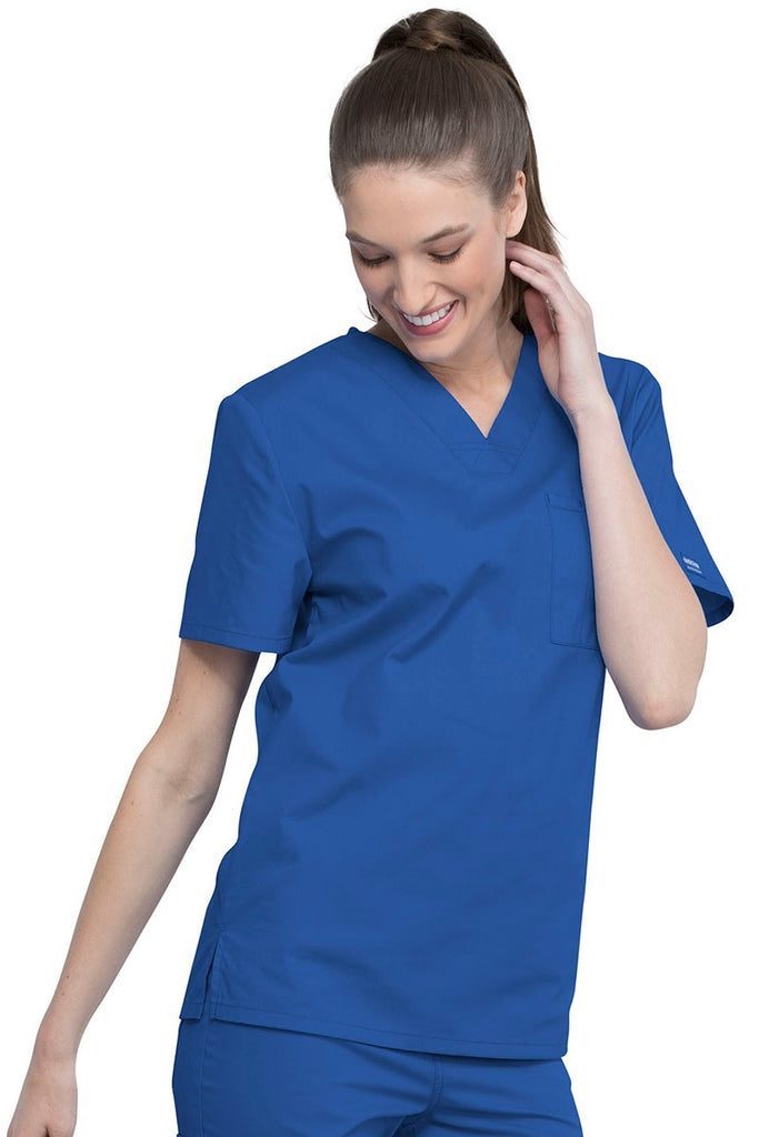 A young female Nurse Practitioner wearing a Cherokee Unisex Tuck-in V-neck Scrub Top in Royal size Large featuring short sleeves & a V-neckline.