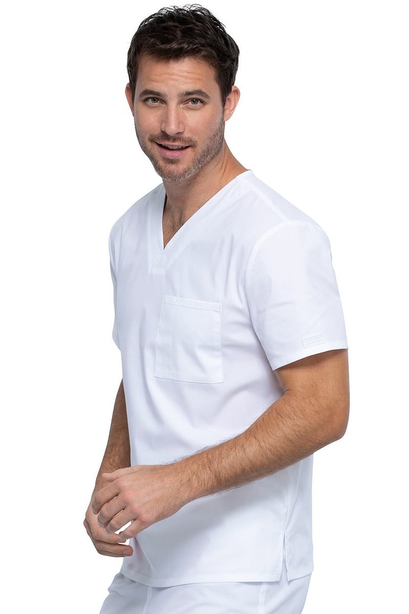 A young male Psychiatric Aide wearing a Cherokee Unisex Tuckable V-neck Scrub Top in White size Medium featuring one front chest pocket with a pen stitch on the wearer's left side.