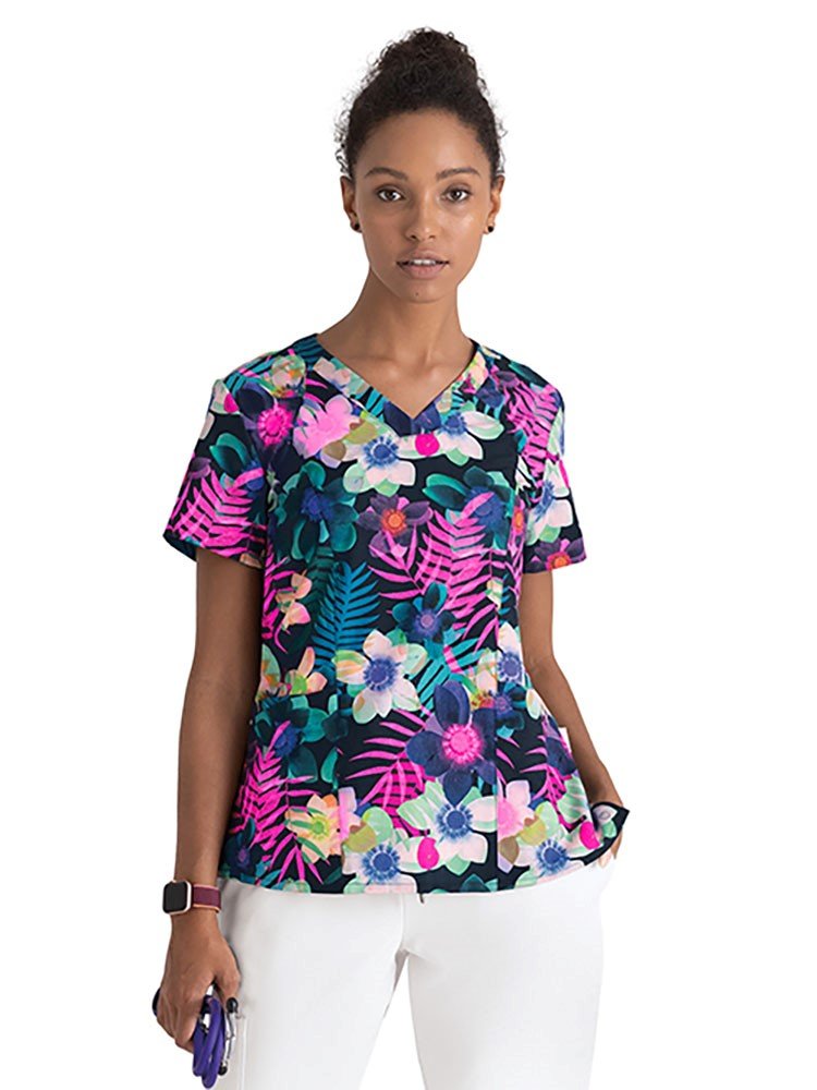 Young female healthcare worker wearing a Barco One Women's Print V-Neck Scrub Top in Summer Delight featuring a modern fit with a total of 3 pockets.