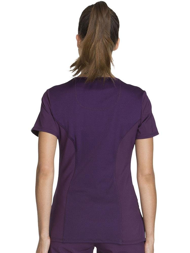 An image of a young female LPN turned around, wearing a Cherokee Infinity Women's Antimicrobial Mock Wrap Top in Eggplant size small.