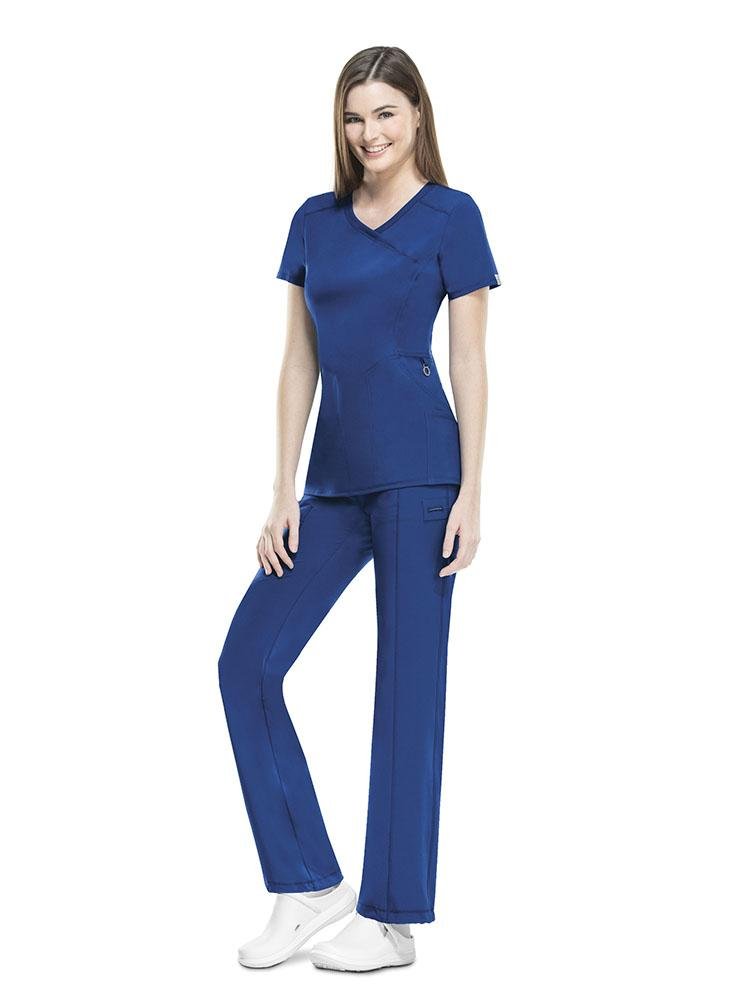 A young female RN wearing a Cherokee Infinity Women's Antimicrobial Mock Wrap Top in Galaxy Blue size medium featuring a Y-neck mock wrap neckline.
