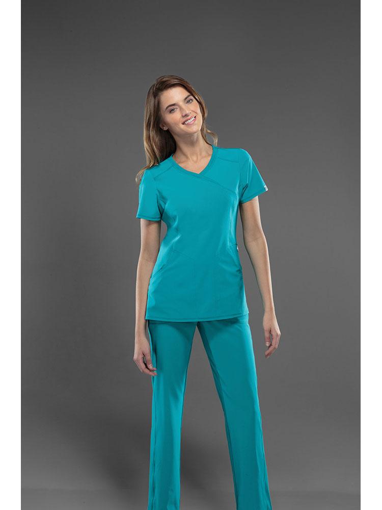 A female Veterinarian wearing a Cherokee Infinity Women's Antimicrobial Mock Wrap Top and matching bottom in Teal featuring a total of 5 pockets.