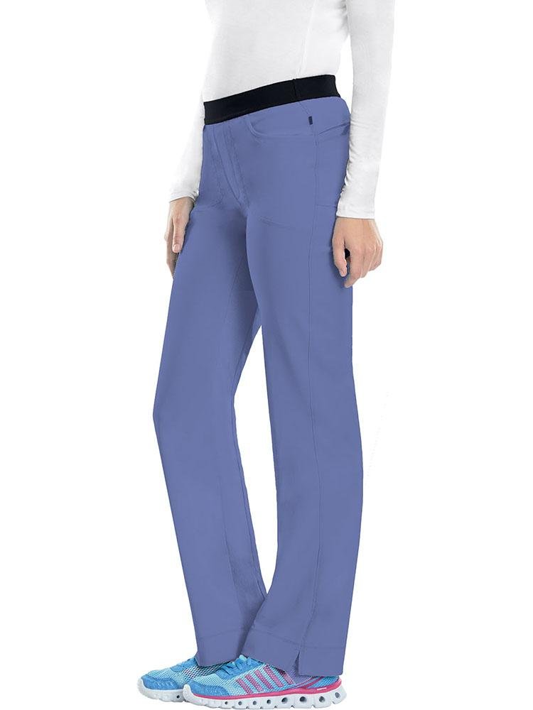 A young female LPN wearing a Cherokee Infinity Women's Low-Rise Slim Pull On Scrub Pant in Ceil size XS Tall featuring a unique moisture-wicking fabric.