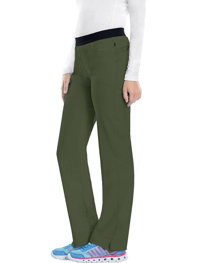 A young female Occupational Therapy Aide wearing a Cherokee Infinity Women's Low-Rise Slim Pull On Scrub Pant in Olive size XS featuring an elastic waistband.