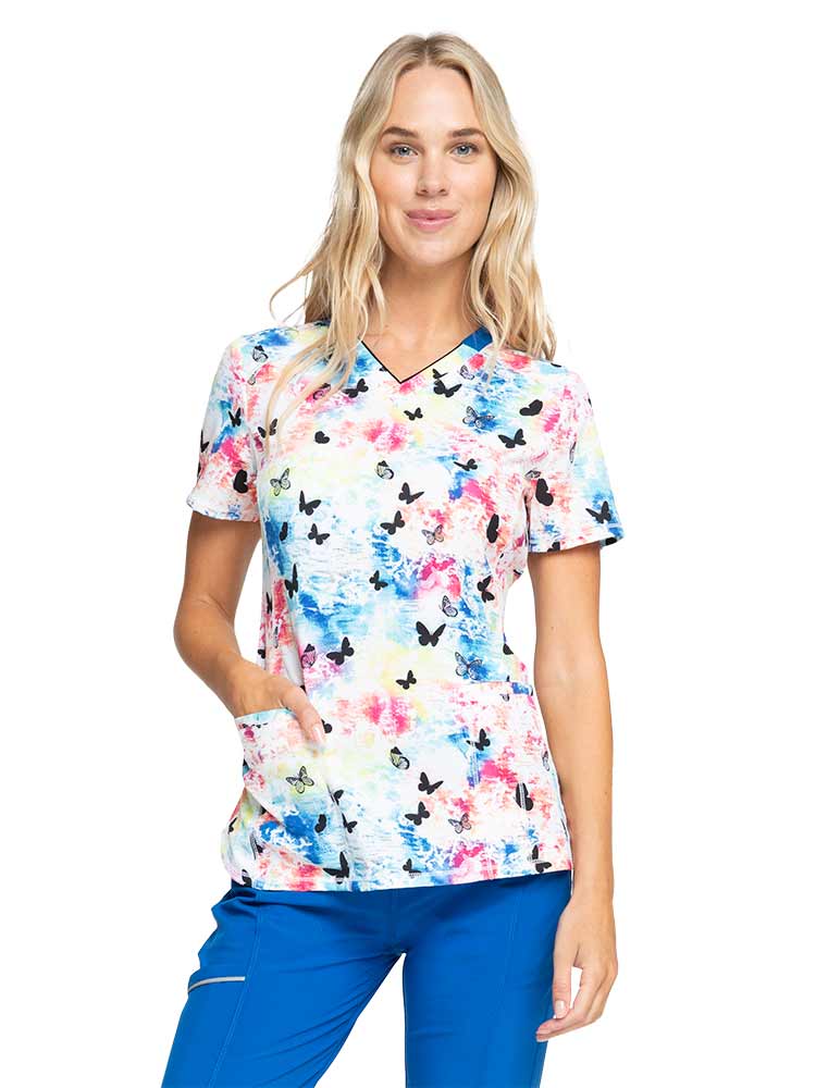 Young woman wearing a Women's Print V-neck Scrub Top from Infinity by Cherokee in "Rainbow Flight".