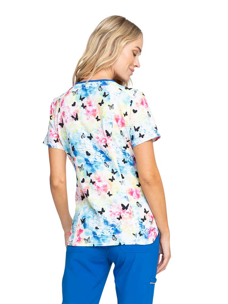 Young nurse wearing a Women's Print V-neck Scrub Top from Infinity by Cherokee in "Rainbow Flight" featuring two front welt pockets & one instrument slot on left.