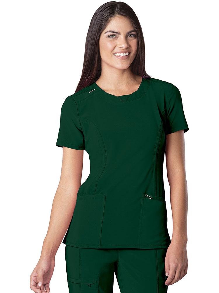 A young female Home Care Health Aide wearing a Cherokee Infinity Women's Round Neck Scrub Top in Hunter size Medium featuring rib-knit insets at the front neckband.