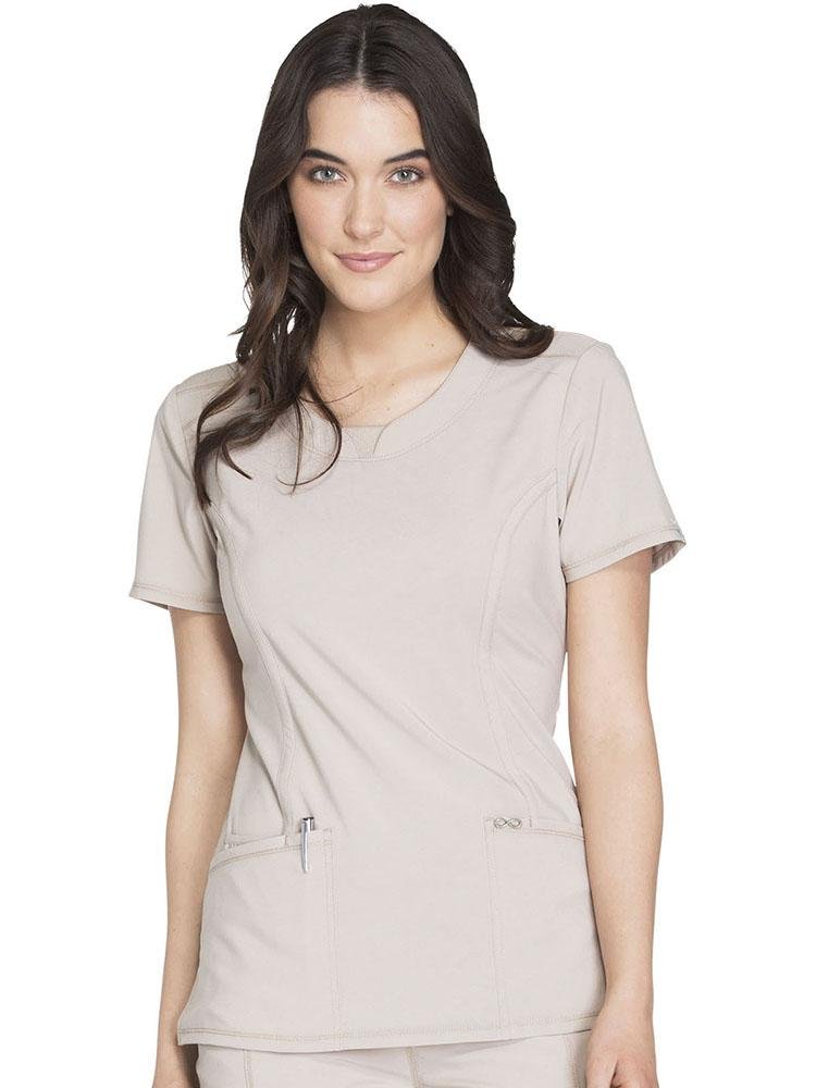 A young female Medical Assistant wearing a Cherokee Infinity Women's Round Neck Scrub Top in Khaki size Medium featuring a contemporary fit & short sleeves.
