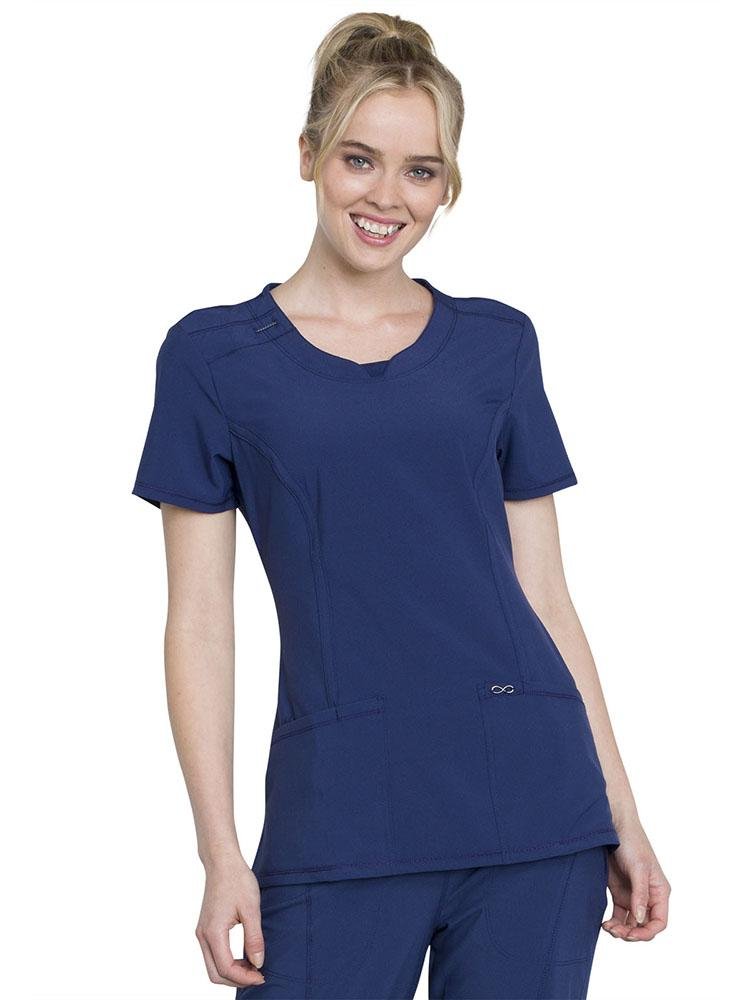 A young female Dental Assistant wearing a Cherokee Infinity Women's Round Neck Scrub Top in Navy size XL featuring a Bungee I.D. badge loop on the right shoulder.