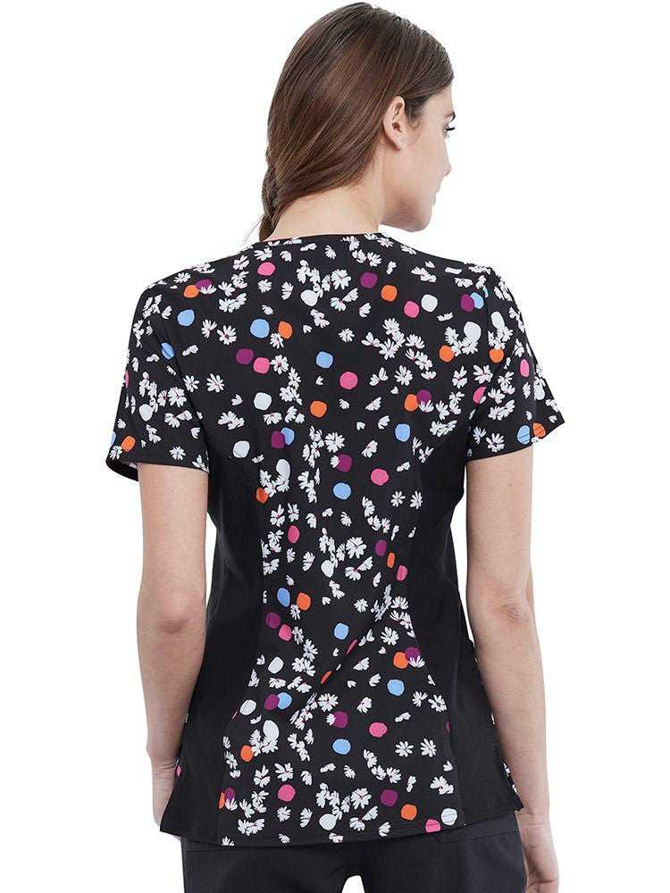Young nurse wearing a Cherokee Women's Knit Panel Print Top in Polka Dot Petals featuring slanted should yoke panels with badge loop.