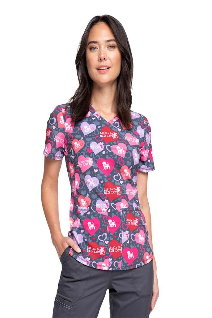 A young female Veterinarian wearing a Cherokee Women's V-neck Print Scrub Top in "Dog is Love" featuring 2 front patch pockets.