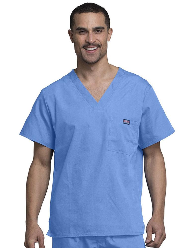 A young male LPN wearing a Cherokee Workwear Originals Men's Solid V-neck Scrub Top in Ceil size 3XL featuring a chests pocket with a pen slot on the wearer's left side .