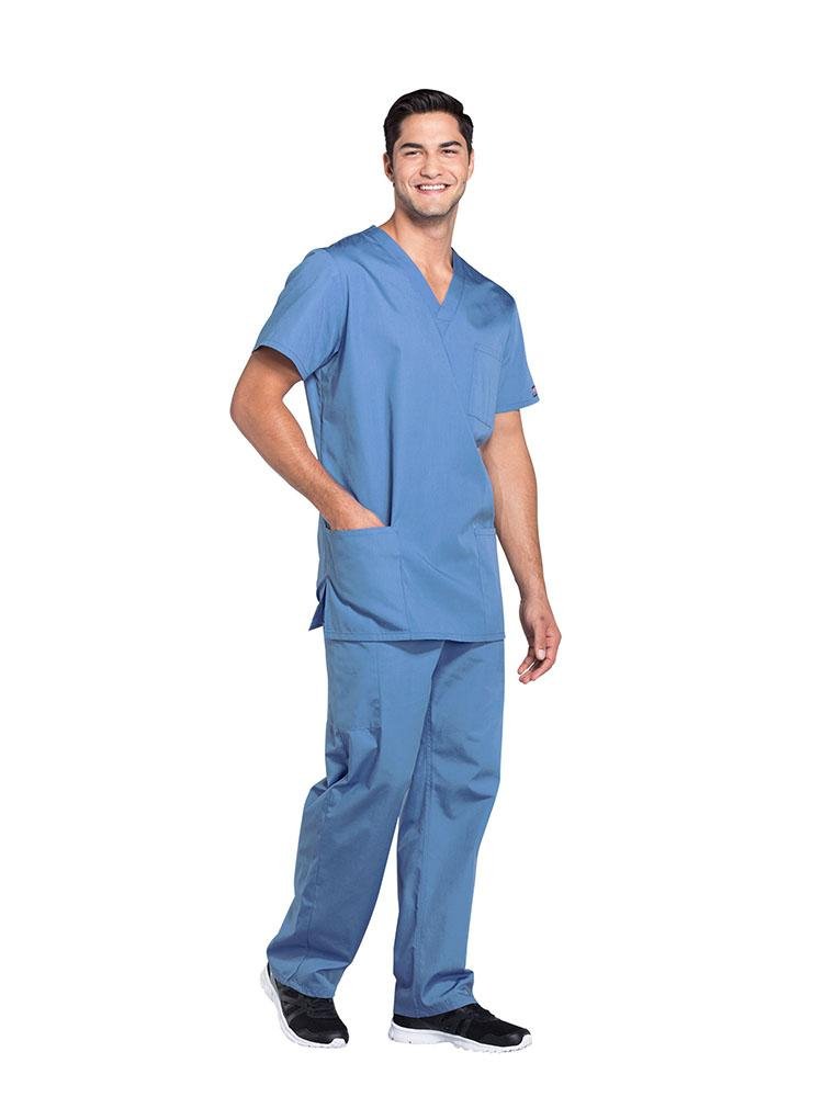 A young male Physical Therapist wearing a Cherokee Workwear Originals Unisex Multi-Pocketed V-neck Scrub Top in Ceil size XL featuring side slits for additional mobility throughout the day.