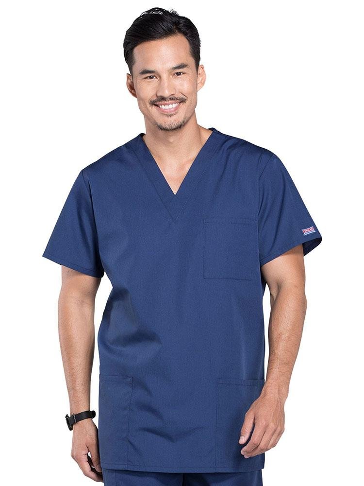 A young male Physician's Assistant wearing a Cherokee Workwear Originals Unisex Multi-Pocket V-neck Scrub Top in Navy size 3XL featuring 2 front patch pockets.