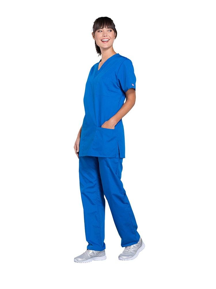 A young female Physical Therapist wearing a Cherokee Workwear Originals Unisex Multi-Pocketed V-neck Scrub Top in Roayl size XL featuring side slits for additional mobility throughout the day.
