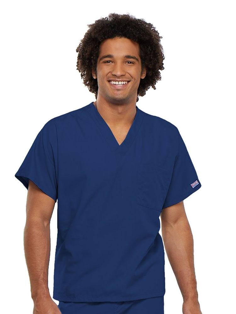 A young male Physician's Assistant wearing a Cherokee Workwear Originals Unisex Single Pocket V-neck Scrub Top in Galaxy Blue size 4XL featuring short sleeves.