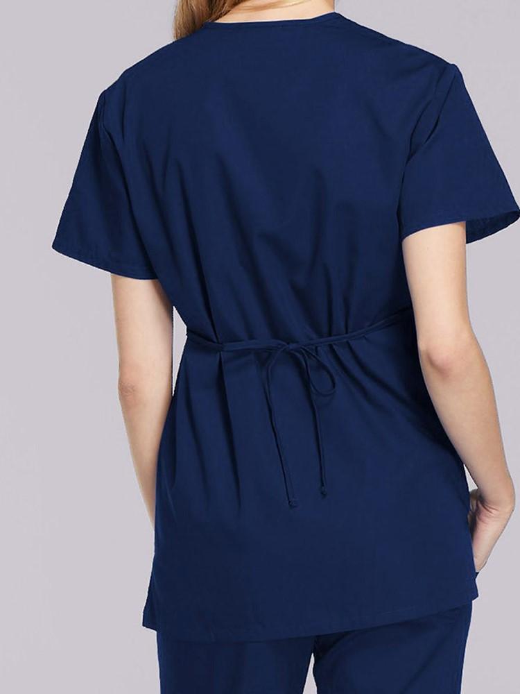 A female LPN wearing a Cherokee Workwear Originals Women's Mock Wrap Scrub Top in Navy size Medium featuring an adjustable tie-back & a center back length of 28.5".
