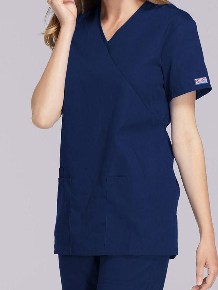 A young female Healthcare Professional wearing a Cherokee Workwear Originals Women's Solid Scrub Top in Navy  size Medium featuring a unique crossover, mock wrap neckline.