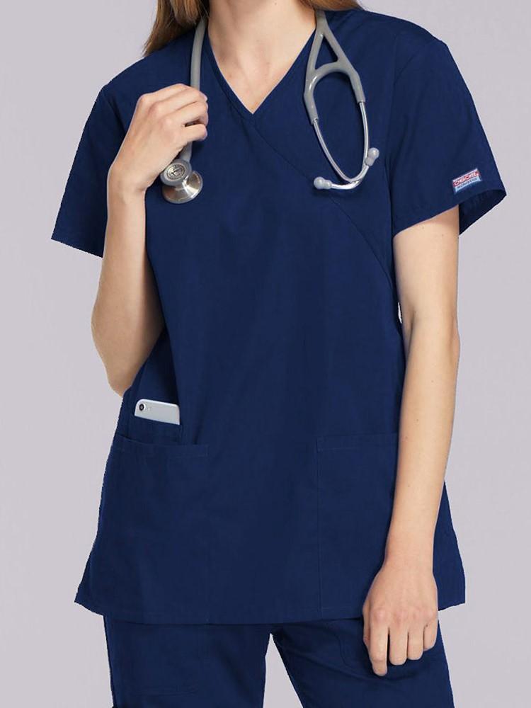 A young female EMT wearing a Cherokee Workwear Originals Women's Mock Wrap Top in Navy  size 2XL featuring short sleeves.