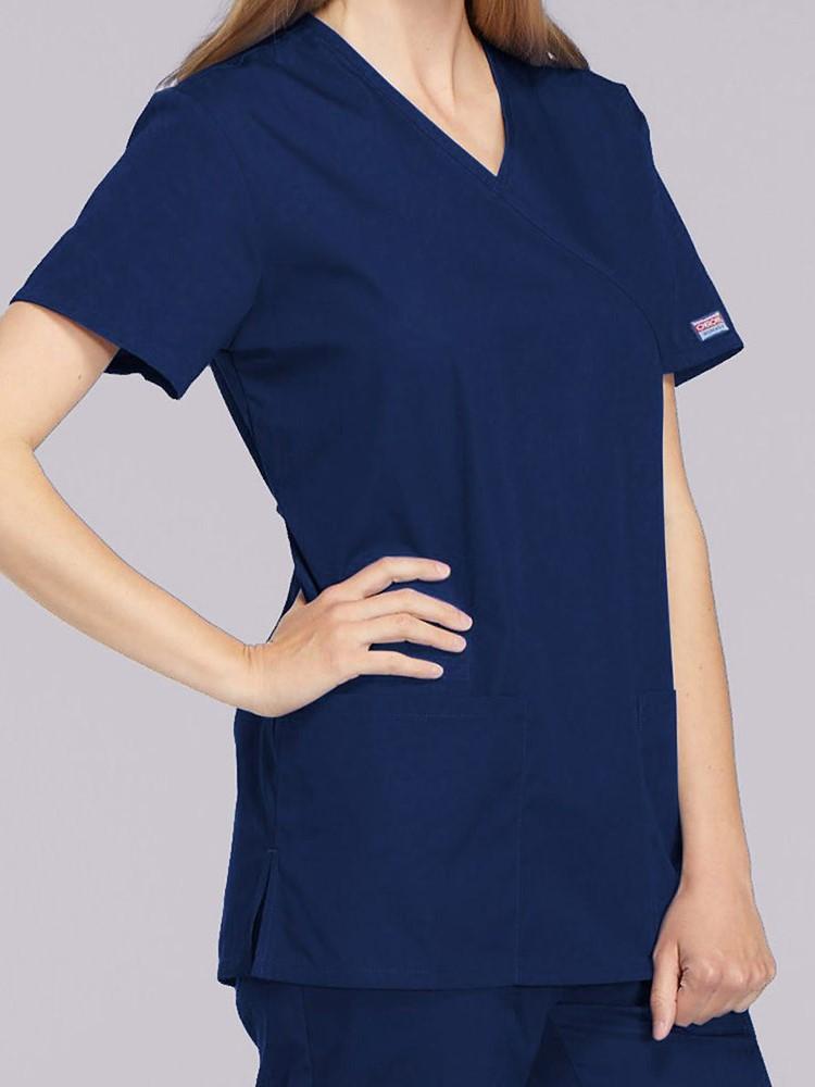 A young female Pharmacist wearing a Cherokee Workwear Originals Women's Mock Wrap Solid Scrub Top in Navy size Small featuring a 2 front patch pockets.