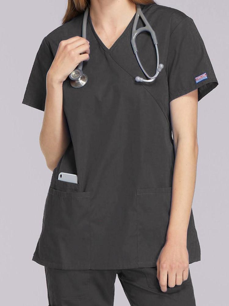 A young female Registered Nurse wearing a Cherokee Workwear Originals Women's Mock Wrap Top in Navy size XL featuring short sleeves.