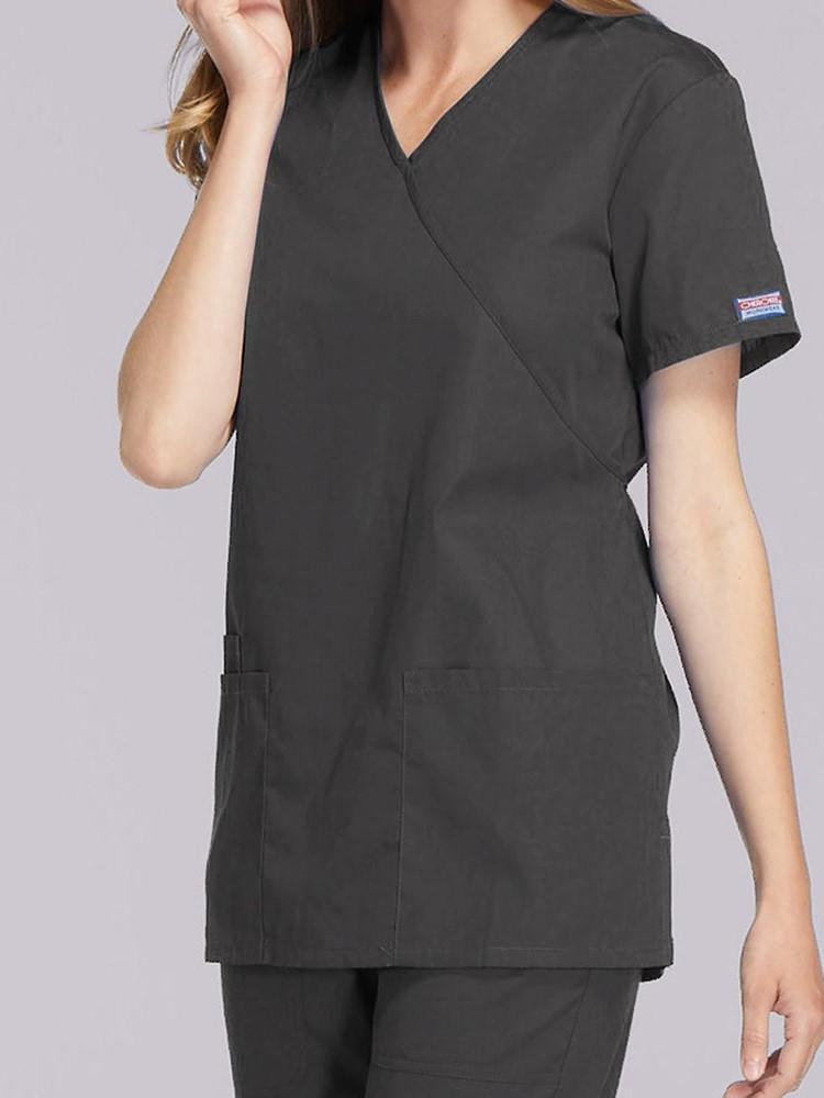 A young female Medical Assistant wearing a Cherokee Workwear Originals Women's Solid Scrub Top in Pewter size Medium featuring a unique crossover, mock wrap neckline.