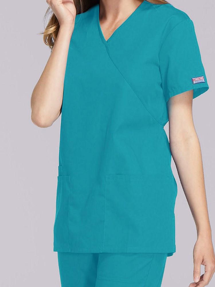 A young female Healthcare Professional wearing a Cherokee Workwear Originals Women's Solid Scrub Top in Tea size Medium featuring a unique crossover, mock wrap neckline.