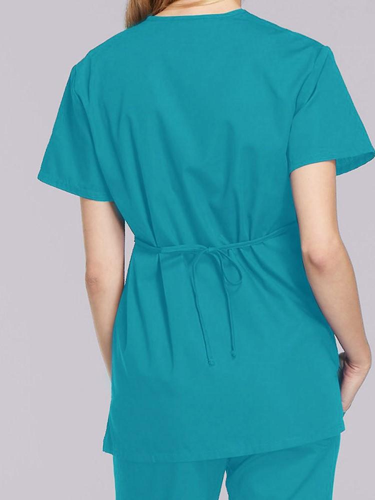 A female LPN wearing a Cherokee Workwear Originals Women's Mock Wrap Scrub Top in Teal size Medium featuring an adjustable tie-back & a center back length of 28.5".