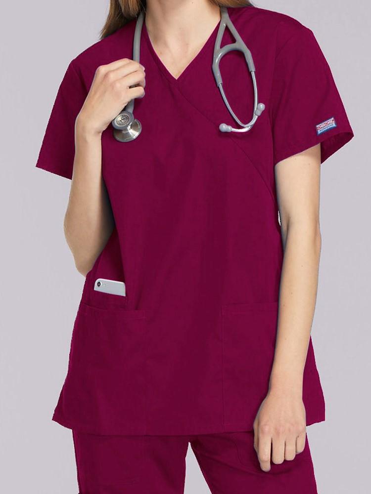 A young female EMT wearing a Cherokee Workwear Originals Women's Mock Wrap Top in Wine size 2XL featuring short sleeves.