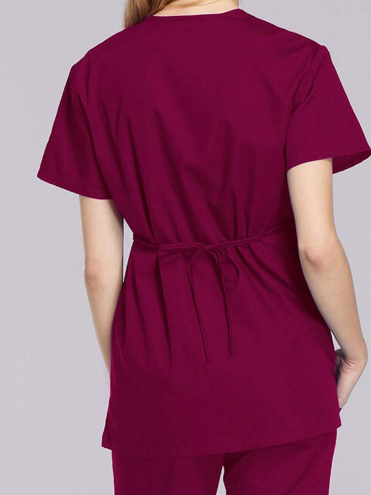 A female LPN wearing a Cherokee Workwear Originals Women's Mock Wrap Scrub Top in Wine size Medium featuring an adjustable tie-back & a center back length of 28.5".