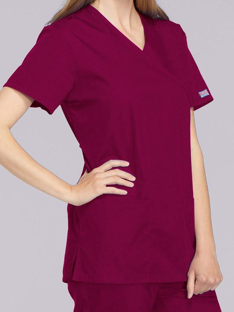 A young female Pharmacist wearing a Cherokee Workwear Originals Women's Mock Wrap Solid Scrub Top in Wine size Small featuring a 2 front patch pockets.