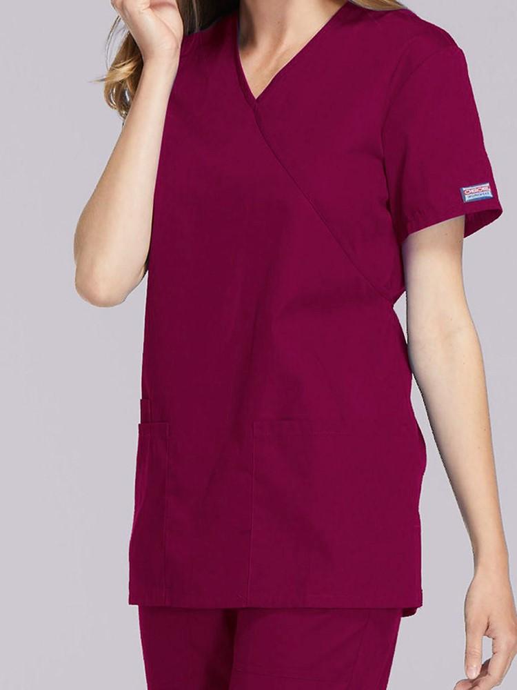 A young female Healthcare Professional wearing a Cherokee Workwear Originals Women's Solid Scrub Top in Wine size Medium featuring a unique crossover, mock wrap neckline.