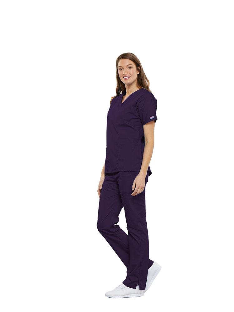 A female Respiratory Therapist wearing a Cherokee Workwear Originals women's Multi-Pocketed V-Neck Scrub Top in Eggplant size medium featuring side seam vents for additional range of motion throughout the day.