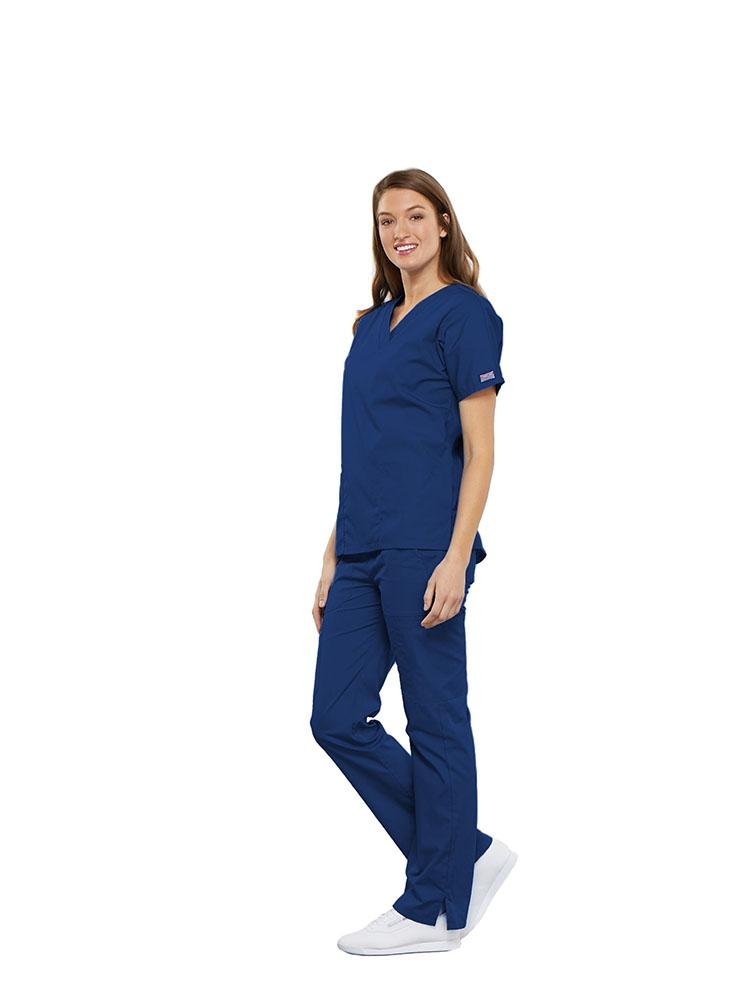 A female Clinical Laboratory Technologist wearing a Cherokee Workwear Originals women's Multi-Pocketed V-Neck Scrub Top in Galaxy Blue size Large featuring side seam vents for additional range of motion throughout the day.