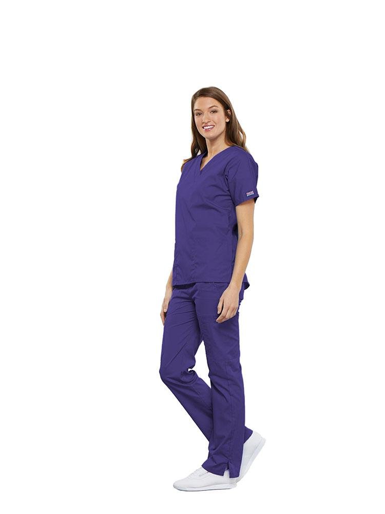 A female Anesthesiologist wearing a Cherokee Workwear Originals women's Multi-Pocketed V-Neck Scrub Top in Grape size medium featuring side seam vents for additional range of motion throughout the day.
