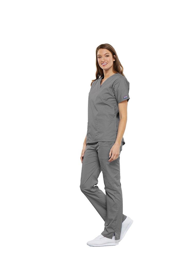 A female Clinical Laboratory Technologist wearing a Cherokee Workwear Originals women's Multi-Pocketed V-Neck Scrub Top in Grey size XS featuring side seam vents for additional range of motion throughout the day.