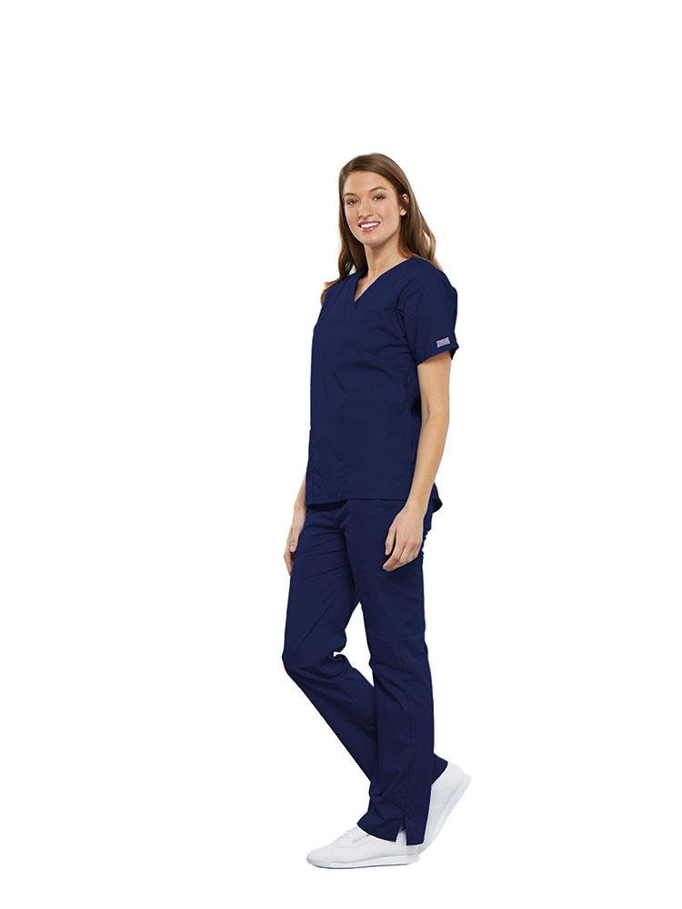 A female Clinical Laboratory Technologist wearing a Cherokee Workwear Originals women's Multi-Pocketed V-Neck Scrub Top in Navy size medium featuring side seam vents for additional range of motion throughout the day.