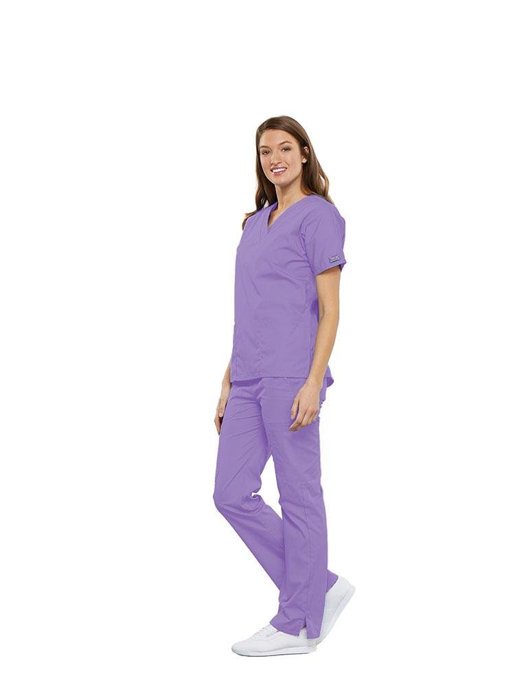 A female Anesthesiologist wearing a Cherokee Workwear Originals women's Multi-Pocketed V-Neck Scrub Top in Orchid size medium featuring side seam vents for additional range of motion throughout the day.