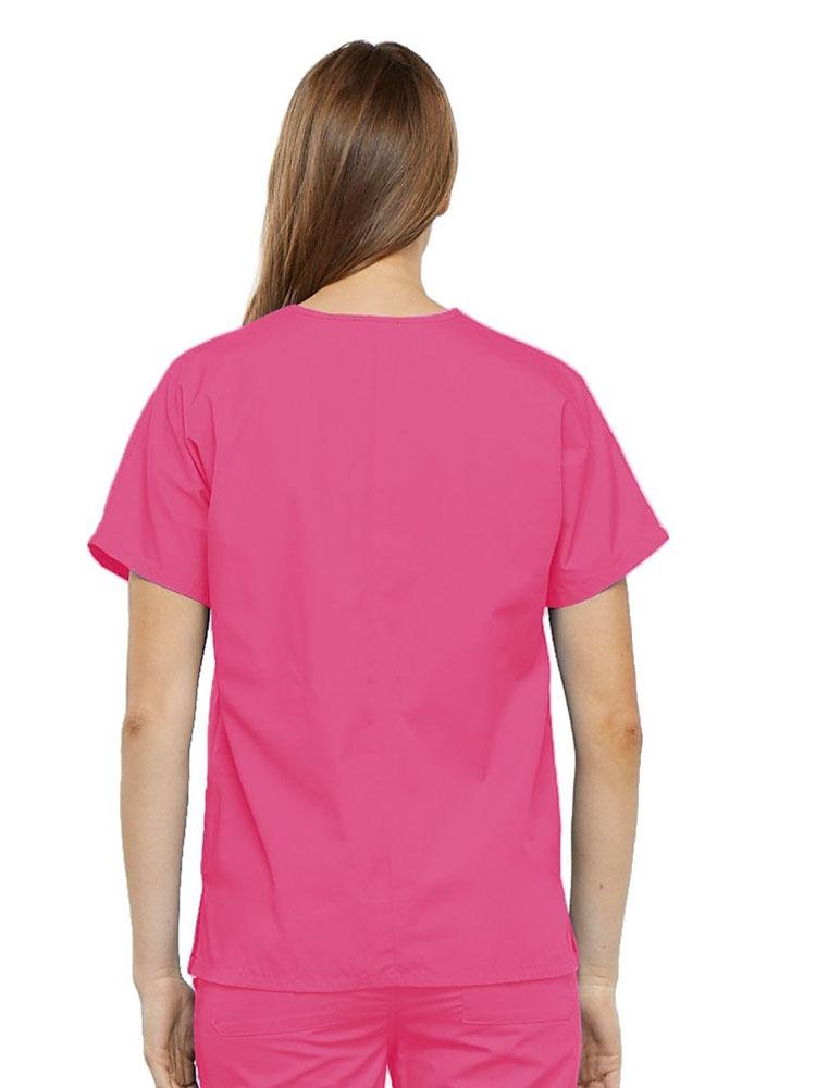 A young female Surgical Technologist wearing a Cherokee Workwear Originals Women's V-neck Scrub Top in Shocking Pink size 2XL featuring a center back length of 26.5".