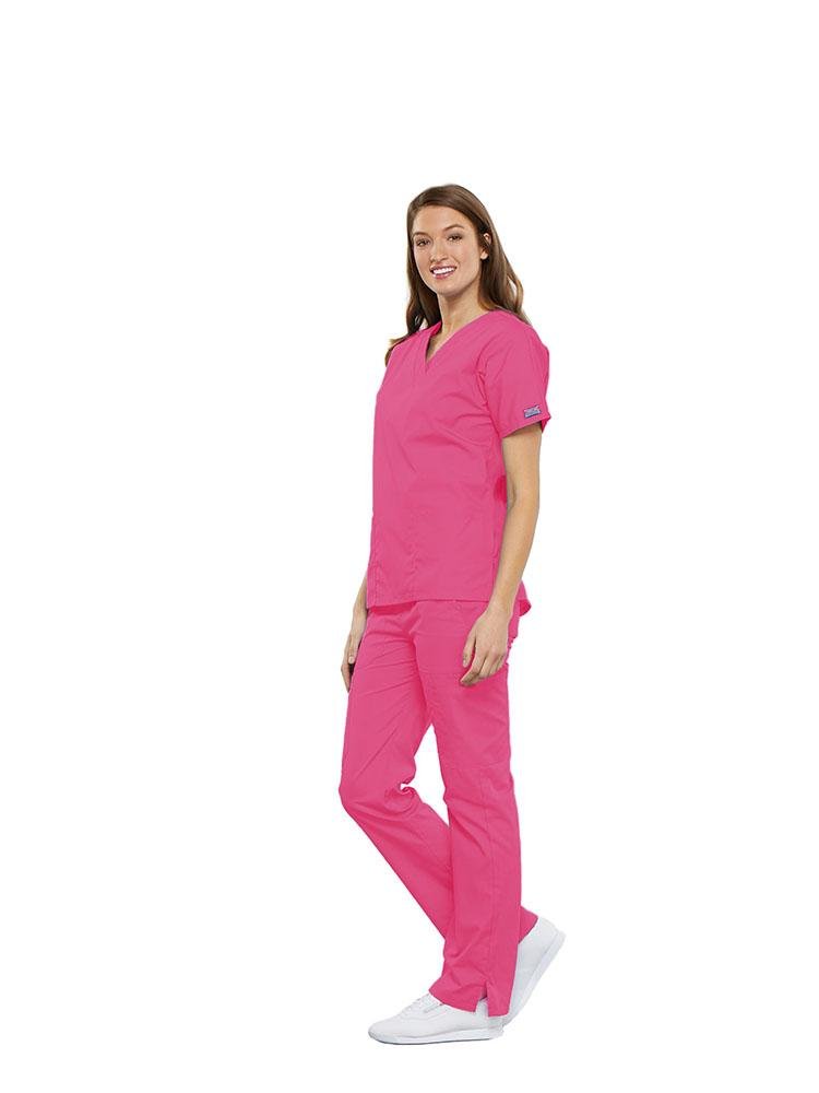 A female Clinical Laboratory Technologist wearing a Cherokee Workwear Originals women's Multi-Pocketed V-Neck Scrub Top in Shocking Pink size Large featuring side seam vents for additional range of motion throughout the day.