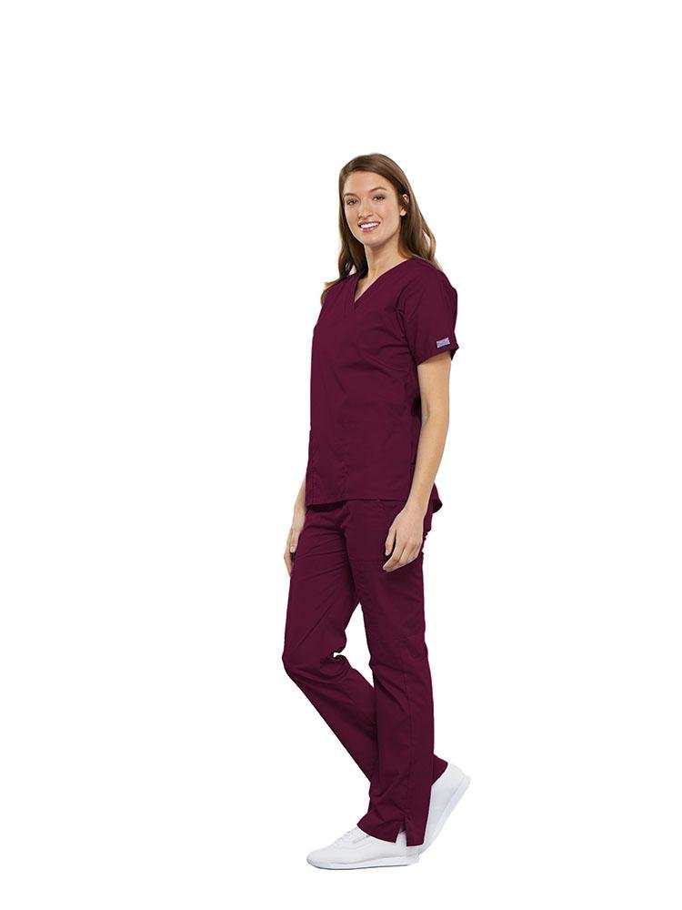A female Anesthesiologist wearing a Cherokee Workwear Originals women's Multi-Pocketed V-Neck Scrub Top in Wine size medium featuring side seam vents for additional range of motion throughout the day.
