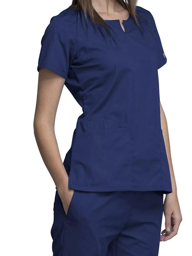 A young female Home Health Aide wearing a Cherokee Workwear Originals Women's Notch Crew Round Neck Scrub Top in Navy size Large featuring side vents for additional range of motion throughout the day.