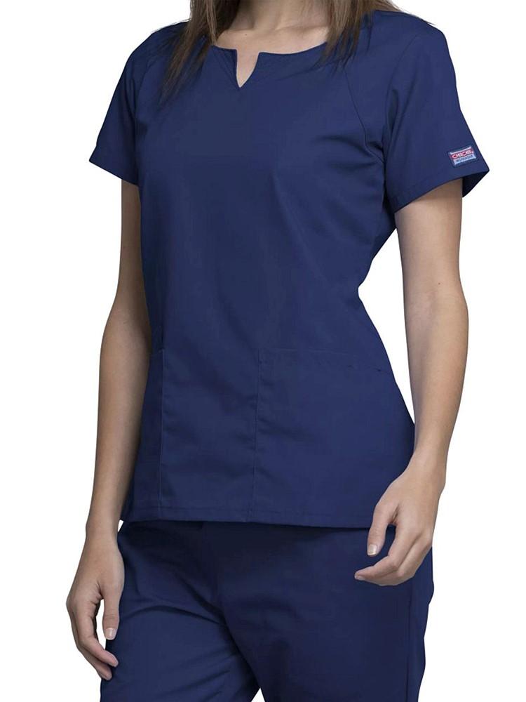 A female Physician's Assistant wearing a Cherokee Workwear Originals Women's Notch Crew Neck Round Neck Scrub Top in Navy size Small featuring a a total of 4 pockets for all of your on the job storage needs. 