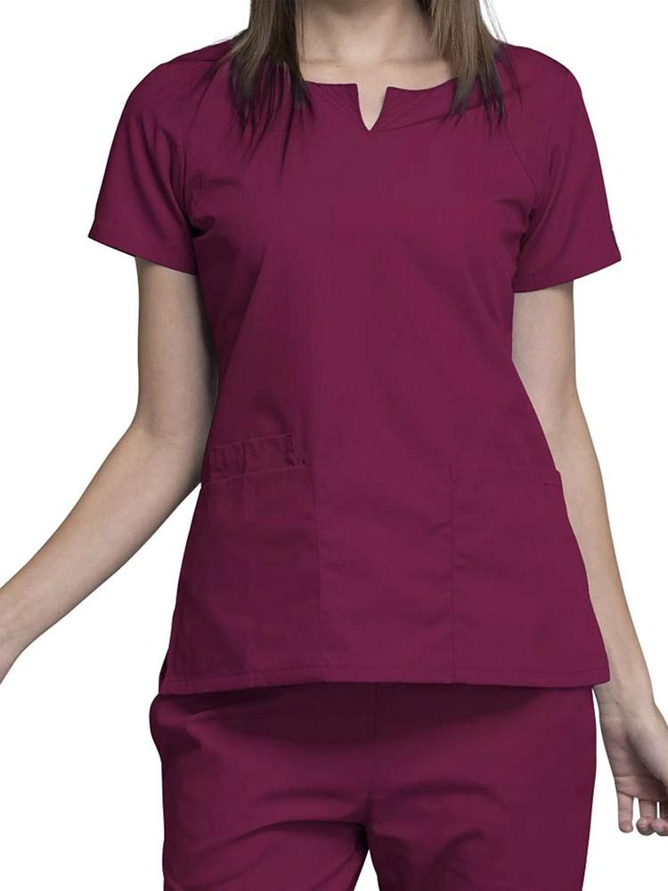 A young female Dental Assistant wearing a Cherokee Workwear Originals Women's Notch Crew Neck Scrub Top in Wine size 2XL featuring a round neckline and curved front neck yokes.