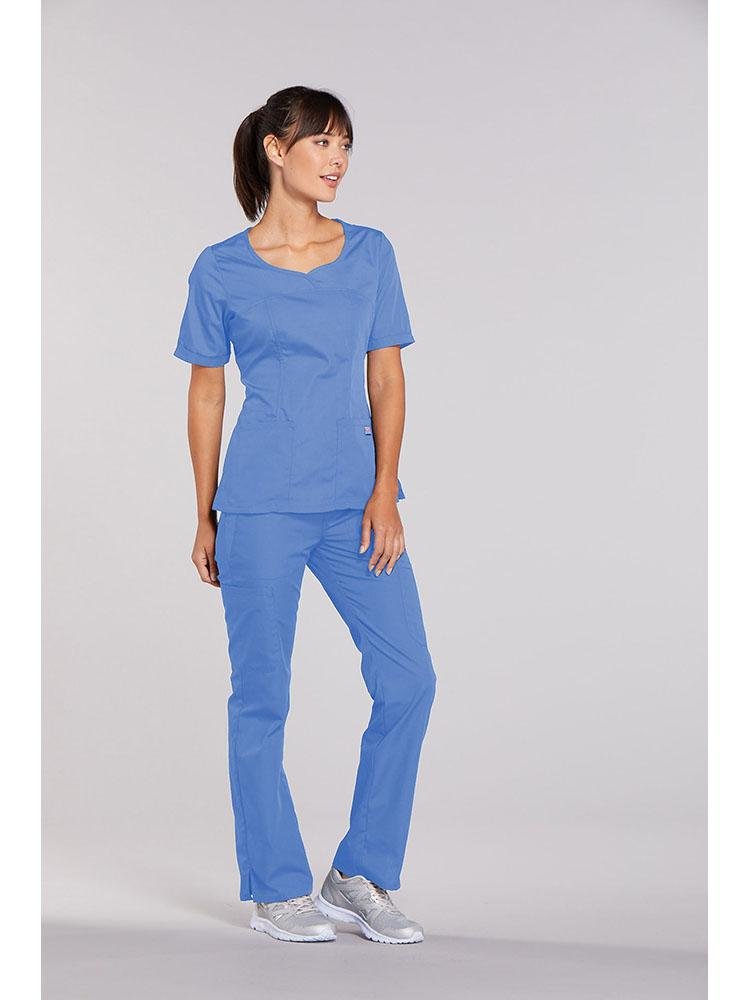 A young female Nurse wearing a Cherokee Workwear Originals Women's Novelty Crossed V-neck Scrub Top in Ceil size small featuring a total of 3 pockets for your on the job storage needs.