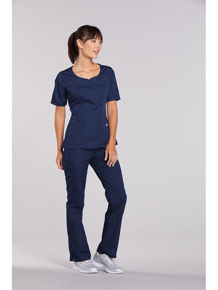 A young female LPN wearing a Cherokee Workwear Originals Women's Novelty Crossed V-neck Scrub Top in Navy size small featuring a total of 3 pockets for your on the job storage needs.