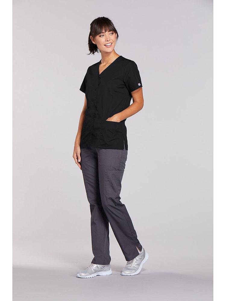 A female Physical Therapist wearing a Cherokee Workwear Originals Women's Snap Front Solid Scrub Top in Black size XL featuring side slots for additional range of motion throughout the day.